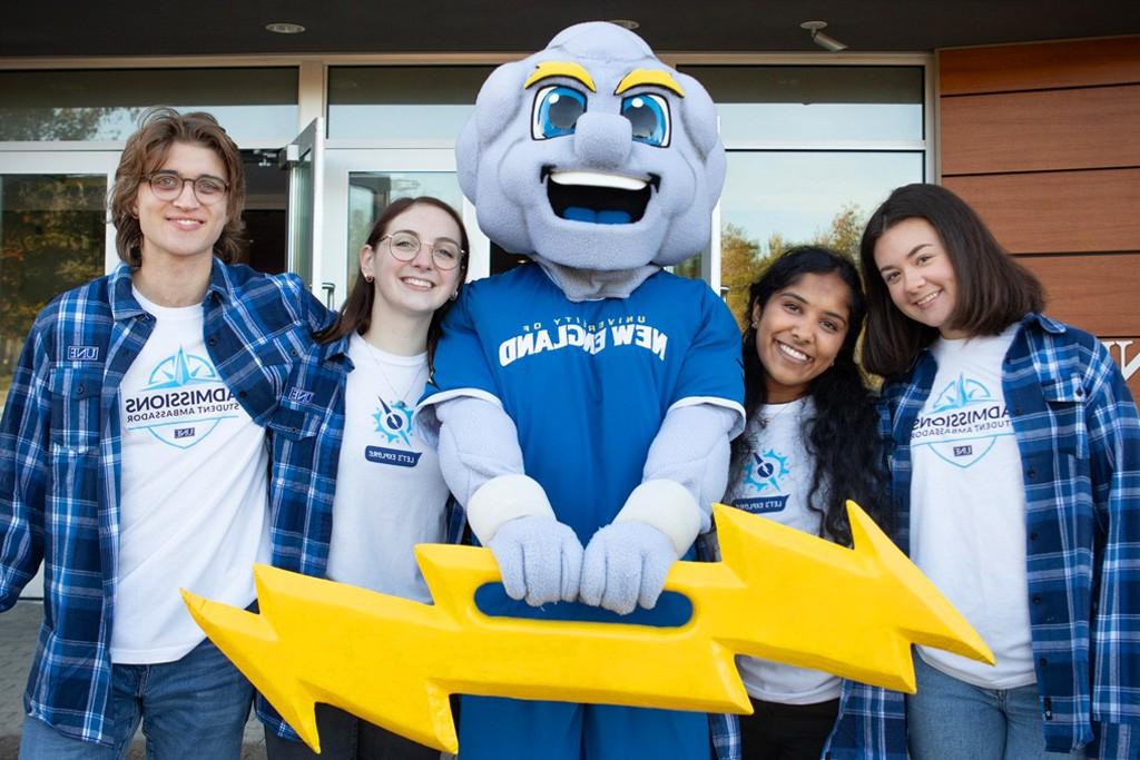 A group of four students wearing matching blue plaid flannels stand around Stormin' Norman